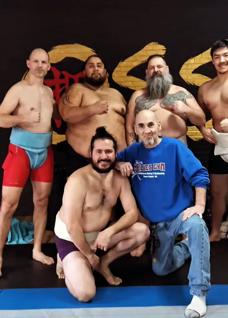 Club members posing with a visitor in front of a gold mural