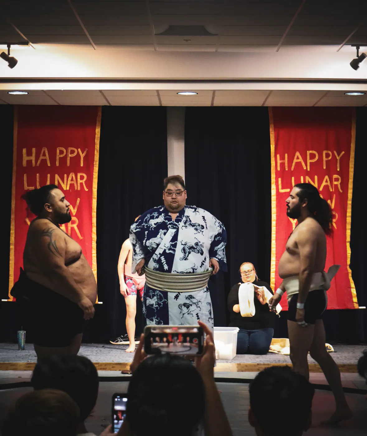 A wrestler in a patterned robe on stage between Happy Lunar New Year banners