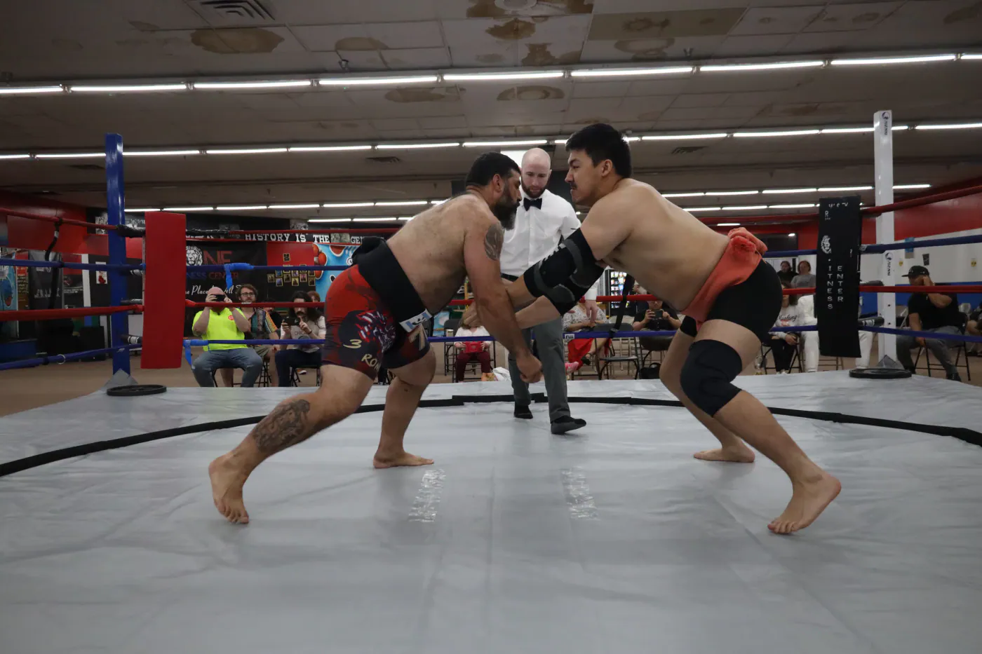 Two wrestlers driving into each other at the charge, with a gyoji behind them