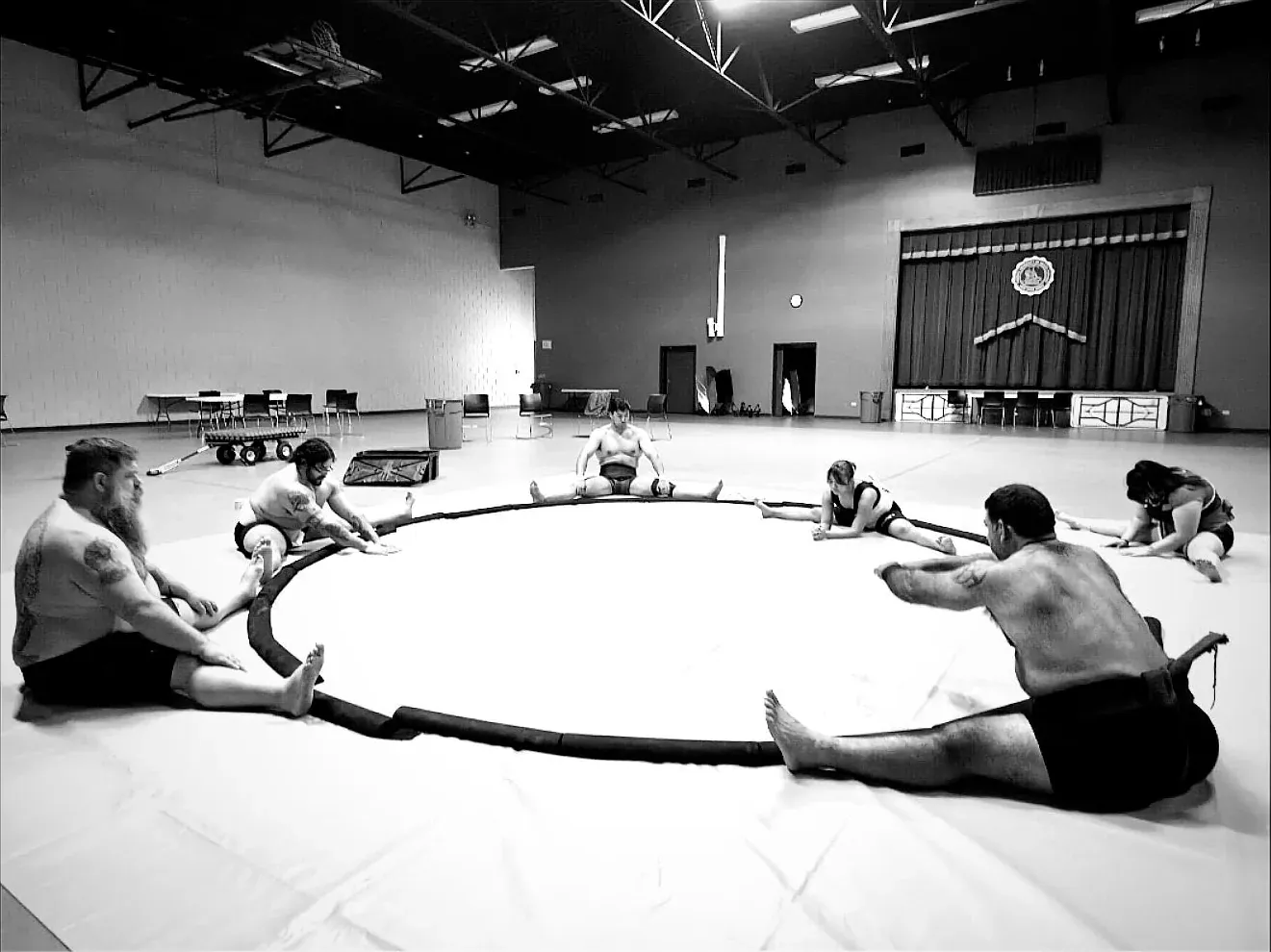Wrestlers sitting in a circle and stretching around the edge of the dohyo